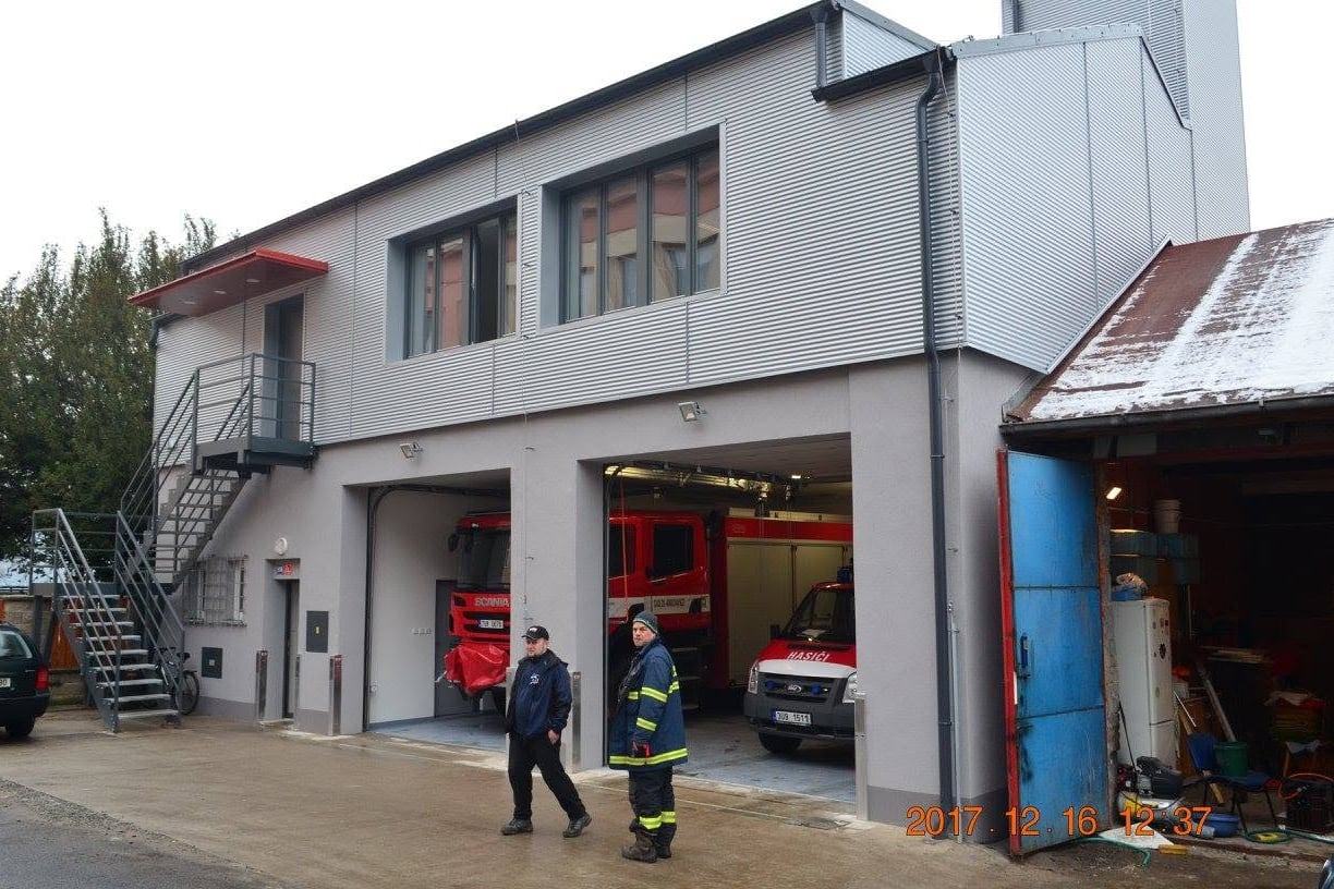 Vjezd do hasičské zbrojnice s červenými vraty a hasičskými vozidly.