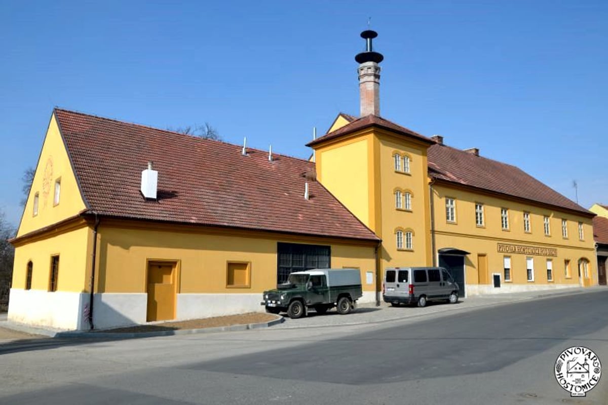 Žlutá budova pivovaru s komínem, auta zaparkovaná u vjezdu.