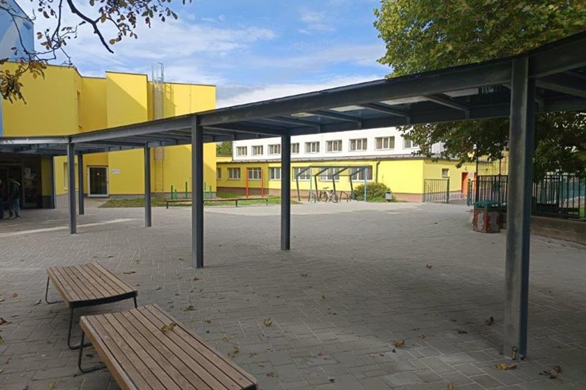 Zastřešené venkovní posezení ve vnitrobloku školy s lavičkami.